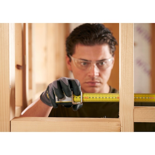 STANLEY FMHT38219-3 tape measure in use, person wearing work gloves measuring wooden frame, close-up photography.