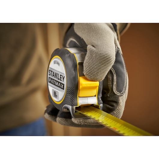 Photo of STANLEY FMHT38219-3 tape measure held in gloved hand, yellow and black with FATMAX label.