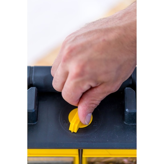 STANLEY FMST81077-1 toolbox close-up, hand turning yellow latch on black lid.