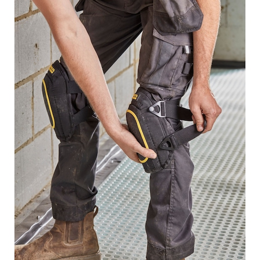 Photo of STANLEY FMST82962-1 black and yellow knee pads being adjusted on work trousers, side angle.