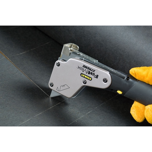 STANLEY PHT350T utility knife cutting black sheet material, close-up angle, gloved hand holding the handle.