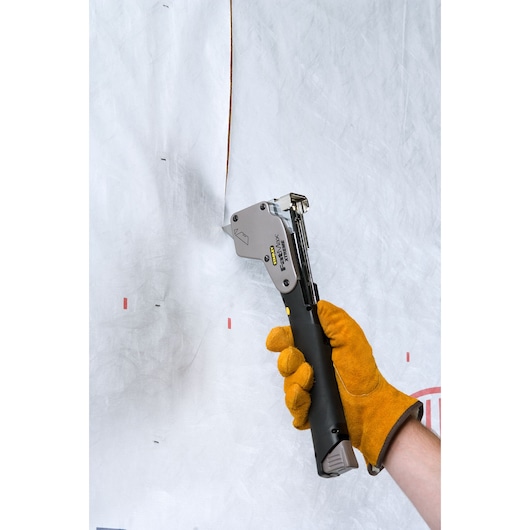Photo of STANLEY PHT350T hammer tacker in use, held by gloved hand, attaching material to wall.