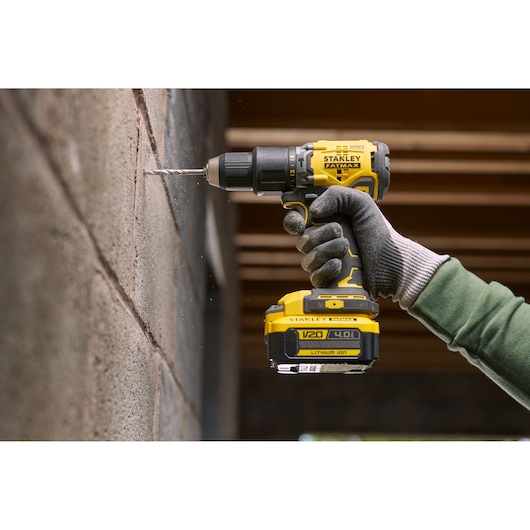 STANLEY SFMCB204 cordless drill in use drilling into a concrete wall, close side view with gloved hand.