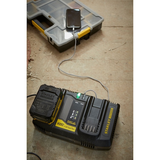 STANLEY SFMCB24 dual port battery charger charging a device, on a workshop floor, angled view.
