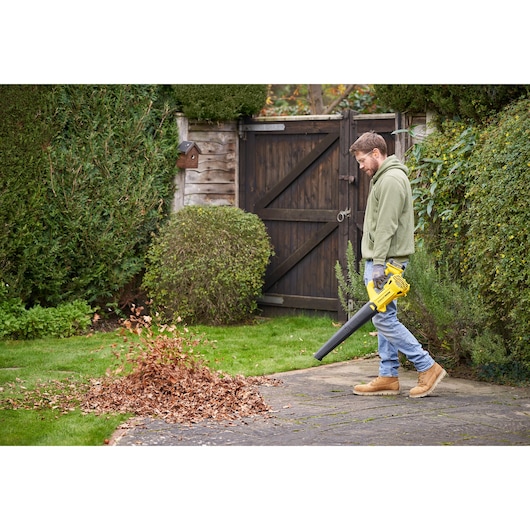 Photo of person using STANLEY SFMCBL714M1 cordless leaf blower to clear leaves from garden patio.