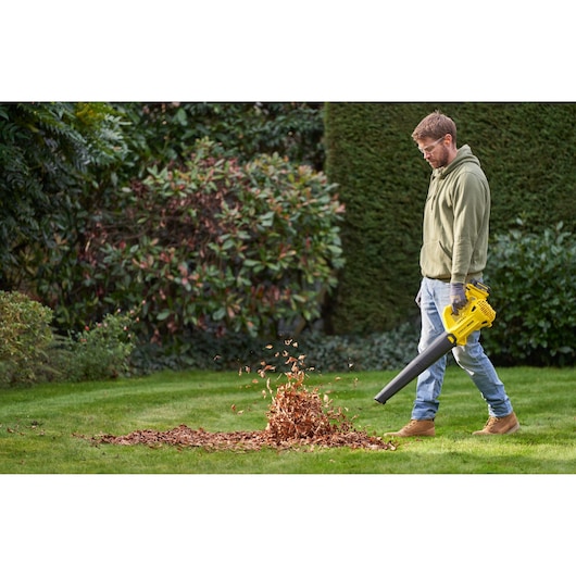 STANLEY SFMCBL714M1 leaf blower in use outdoors, blowing leaves on a green lawn.