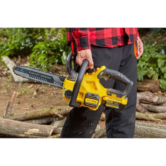 Photo of STANLEY SFMCCS630M1 cordless chainsaw held outdoors, yellow and black, V20 battery visible.