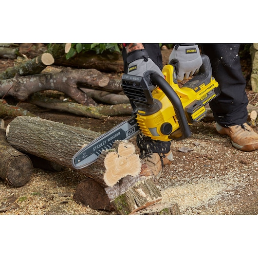 Photo of STANLEY SFMCCS630M1 yellow cordless chainsaw in use cutting log outdoors.