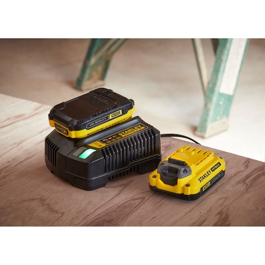 Photo of STANLEY SFMCD700D2S battery charger and battery, yellow and black, on wooden surface.