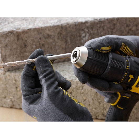 STANLEY SFMCD711B cordless drill close-up, gloved hands inserting drill bit, outdoor setting.