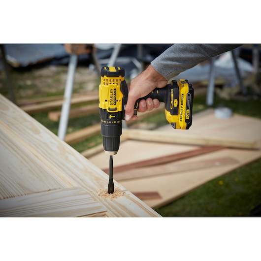 STANLEY SFMCD711DM2 cordless drill in use, drilling into light wood outdoors.