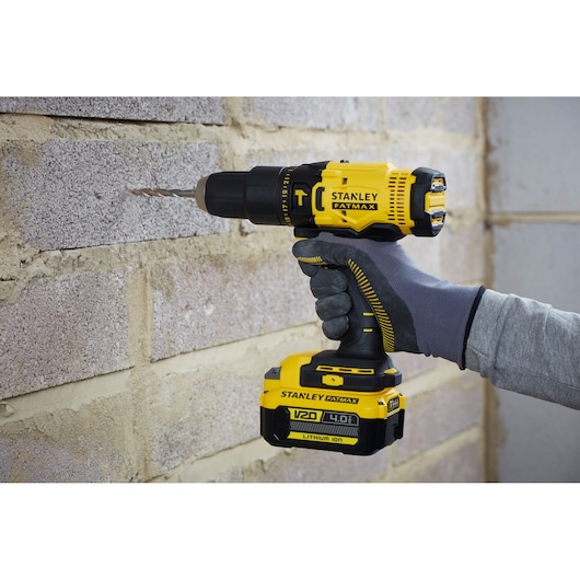 Stanley SFMCD711M1 cordless drill in use on a brick wall, side view, yellow and black, V20 4.0Ah battery.