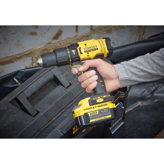 Photo of STANLEY SFMCD711M1 cordless drill driver held in hand, shown near a black tool box.