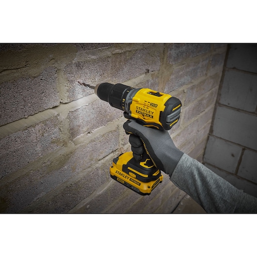 Photo of STANLEY SFMCD715D1A cordless drill being used on a brick wall, yellow and black tool in hand.