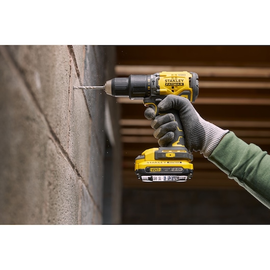 Photo of STANLEY SFMCD715D1A cordless drill, yellow and black, used to drill into a concrete wall.