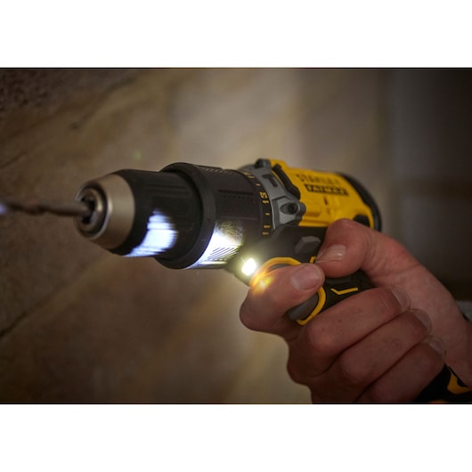 Photo of STANLEY SFMCD715D1A cordless drill in use, yellow and black, with LED light, close-up side view.