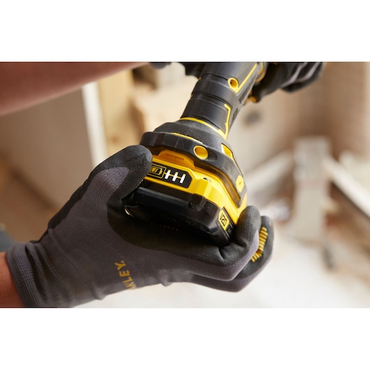 STANLEY SFMCD720DR2 cordless drill close-up in gloved hands, showing battery indicator, construction background.