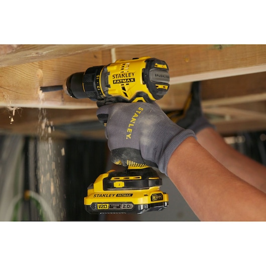 Stanley SFMCD720DR2 brushless cordless drill in use under wooden beam, yellow and black design.