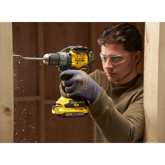 Photo of STANLEY SFMCD725B cordless drill in use, drilling into wood, yellow and black design.