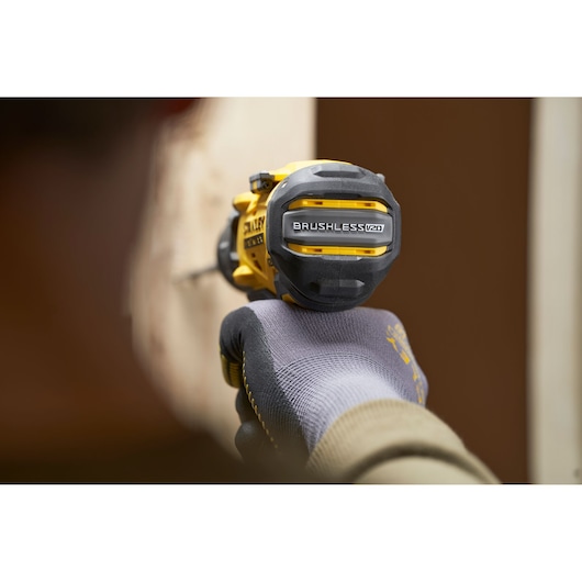 STANLEY SFMCD725B brushless drill in use, close-up view held by gloved hand against a light wall.