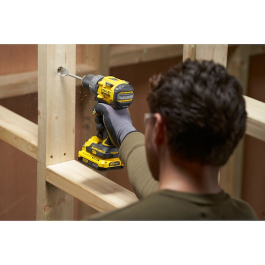 STANLEY SFMCD725D2K cordless drill in use drilling wood, construction setting, side angle.