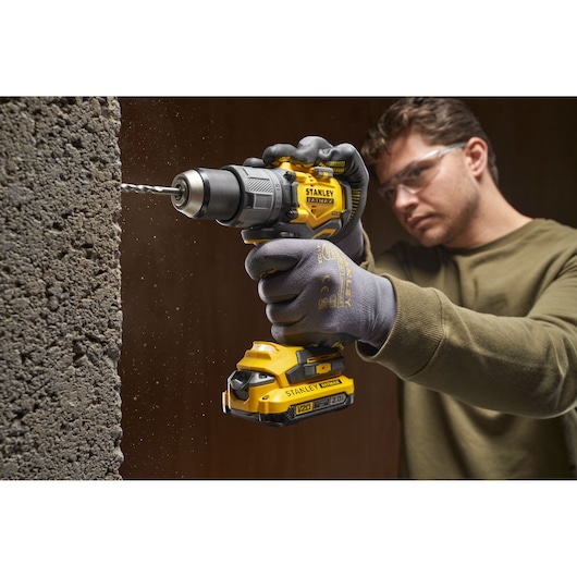 Photo of STANLEY SFMCD726D2K cordless drill in use, drilling into concrete wall, visible V20 battery.