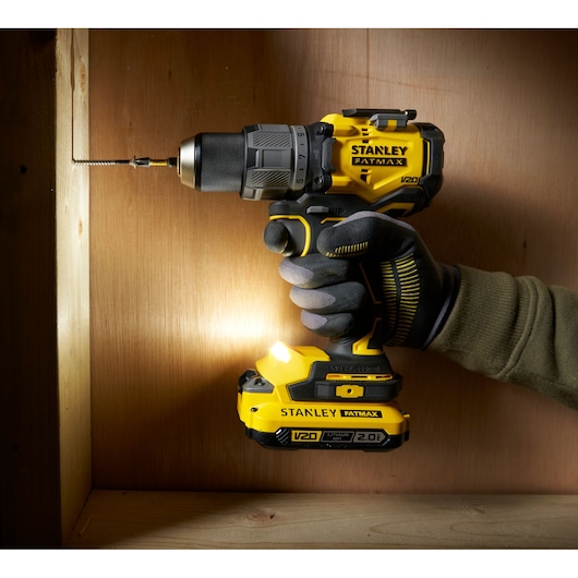 Stanley SFMCD726D2K cordless drill held by gloved hand, drilling into wood, side angle.