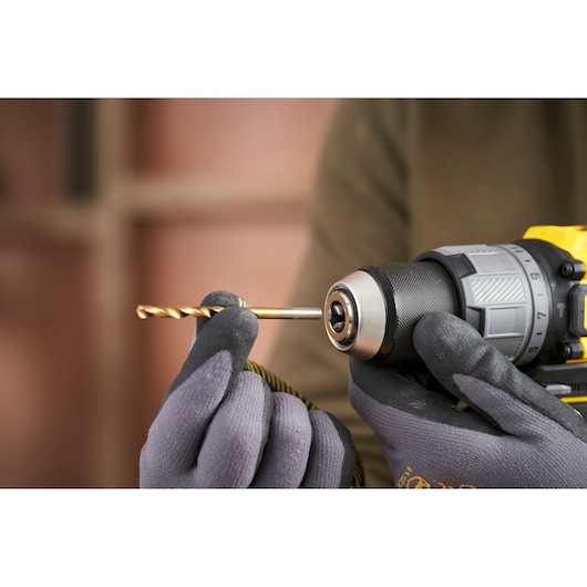 STANLEY SFMCD726D2K drill close-up, gloved hand inserting twist drill bit, photography.
