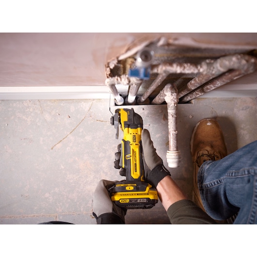 Photo of STANLEY SFMCE510B oscillating multi-tool cutting beside pipes on a concrete floor.