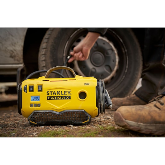 STANLEY SFMCE520B portable yellow tire inflator in use beside vehicle wheel outdoors.