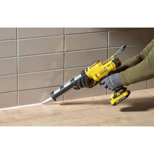 STANLEY SFMCE600B cordless caulking gun in use sealing a joint between a wood counter and tiled wall.