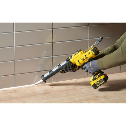 Stanley SFMCE600B cordless caulking gun applying sealant along a tiled wall and wooden surface.