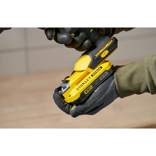 Photo of STANLEY SFMCE600B yellow cordless tool in gloved hands, close-up side view.