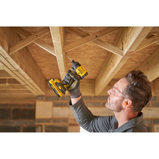 Photo of person using STANLEY SFMCF811B-XJ cordless drill to fasten screw into wooden ceiling frame.