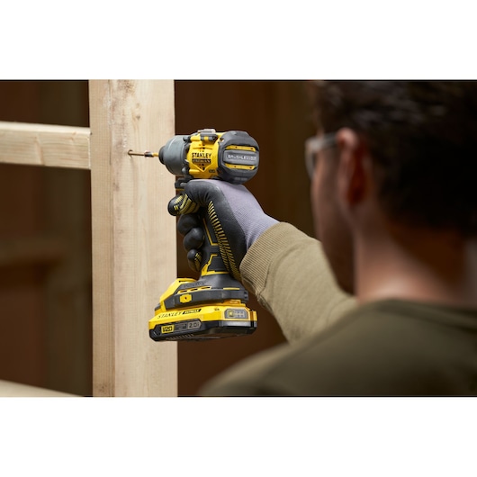 Photo of STANLEY SFMCF830D2K cordless V20 impact driver being used to drive a screw into wood, close-up angle.