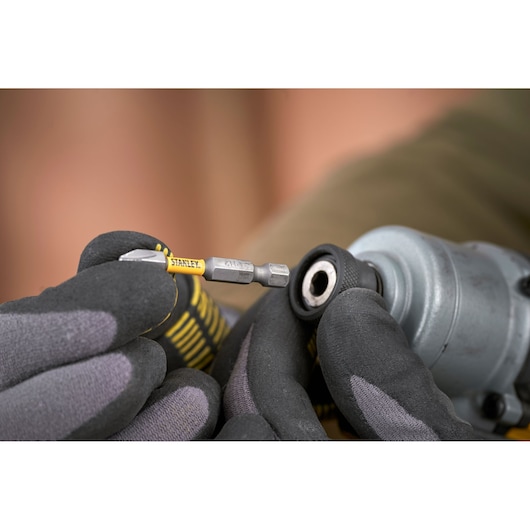 Photo of STANLEY SFMCF830D2K bit being inserted into power tool by gloved hands, close-up.