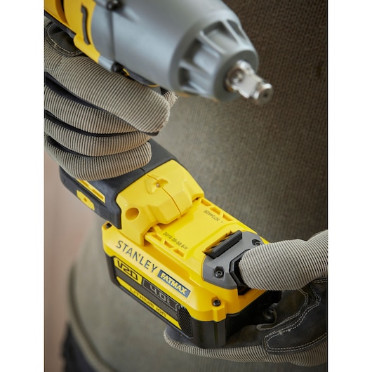 Photo of gloved hands holding STANLEY SFMCF900B cordless impact wrench with V20 FATMAX battery, close-up angle.