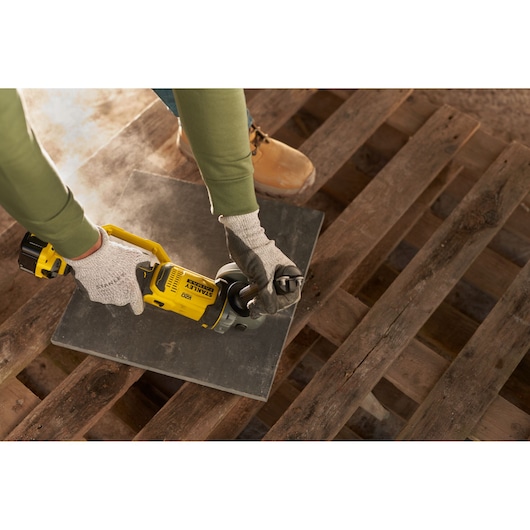 Photo of STANLEY SFMCG400M1S angle grinder in use on a tile, handheld, with gloves, on a wooden pallet.