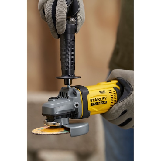 Photo of STANLEY SFMCG400M1S angle grinder with yellow and black housing, held by gloved hands.