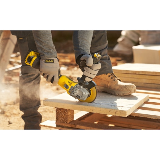STANLEY SFMCG710B-XJ angle grinder in use, grinding stone slab outdoors, close-up view with gloves.