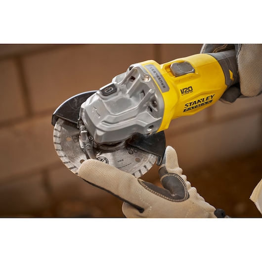 STANLEY SFMCG710B-XJ angle grinder with V20 branding held by gloved hands, close-up view.
