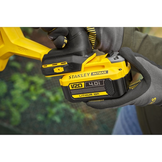 Photo of STANLEY FATMAX SFMCGA75B V20 4.0Ah lithium-ion battery attached to tool, held with gloved hands.