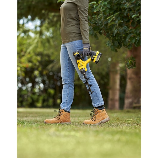 Photo of STANLEY SFMCGA75M1 cordless garden auger held by person outdoors, focus on tool and lower body.