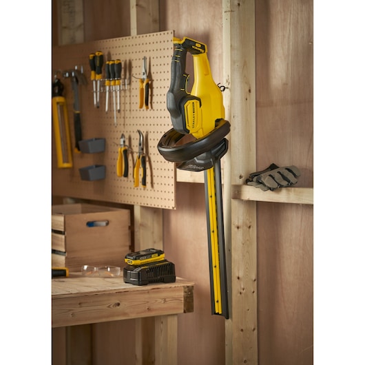 STANLEY SFMCHT650D1 hedge trimmer in a workshop, yellow and black, near tools and charger.