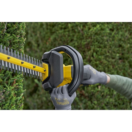 STANLEY SFMCHT655B hedge trimmer closeup in use, yellow body, black handle, trimming green hedge.