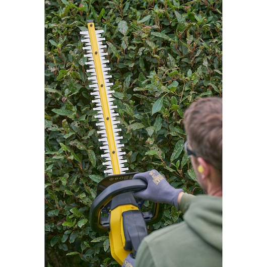 STANLEY SFMCHT655B hedge trimmer in use, close-up of blade cutting green bush outdoors.