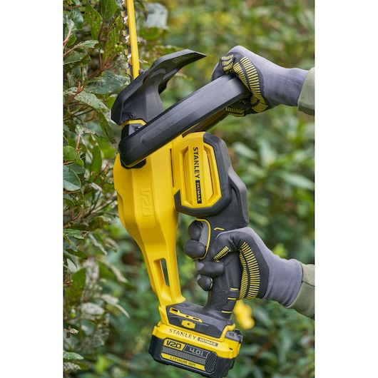 Stanley SFMCHT655B cordless hedge trimmer in use, yellow and black, close-up side angle.
