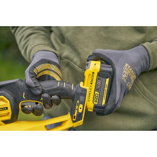 STANLEY SFMCHT655B cordless tool close-up, yellow and black color, held by gloved hands outdoors.