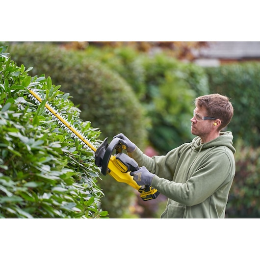 STANLEY SFMCHT655M1 hedge trimmer in use outdoors, trimming green hedges.