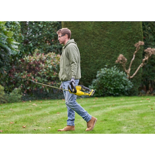 Photo of STANLEY SFMCHT655M1 hedge trimmer held by person in garden, featuring yellow and black design.